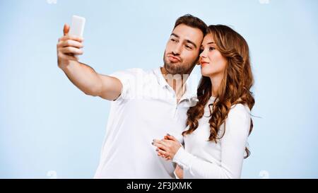 Lächelndes Paar nimmt Selfie isoliert auf blau Stockfoto