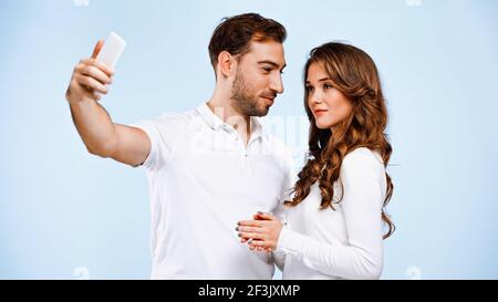 Junger Mann, der Frau ansieht, während er Selfie isoliert auf nimmt Blau Stockfoto