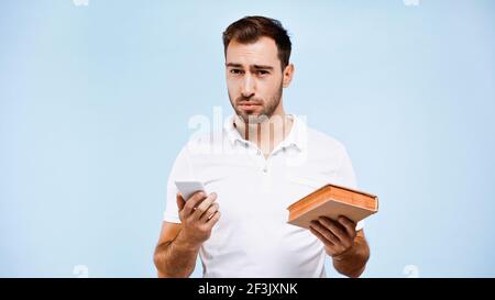 Mann in T-Shirt hält Buch und Smartphone isoliert auf blau Stockfoto