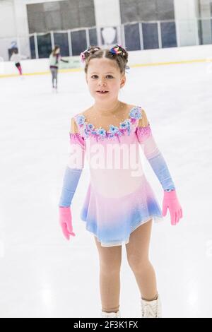 Kleines Mädchen, das Eiskunstlauf auf einer Indoor-Eisbahn übt. Stockfoto