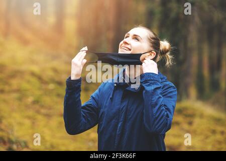 Glückliche Frau entfernen Gesichtsmaske und atmen frische Luft im Park. Pandemie Ende, normales Leben Konzept Stockfoto