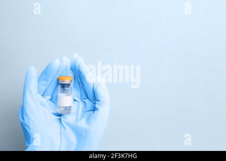 Hand in medizinischen blauen Handschuh mit Flasche Coronavirus-Impfstoff auf blauem Hintergrund. Impfkonzept für die Bevölkerung, Aufschrift Covid 19-Impfstoff Stockfoto