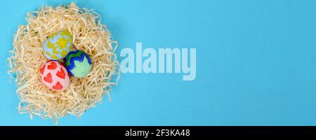 Bunte traditionelle handbemalte Ostereier im Nest isoliert auf blauem Hintergrund. Draufsicht, Kopierbereich, Banner Stockfoto