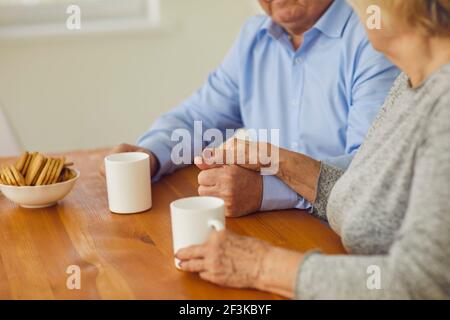 Nahaufnahme am Morgen Seniorenpaar hält Hände am Tisch sitzen und trinken Tee. Stockfoto