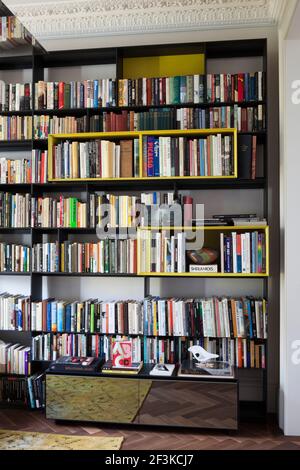 Das schwarz-gelbe Regalsystem B&B Italia beherbergt einen Teil der riesigen Büchersammlung im Morgan House in Notting Hill, London, Großbritannien. Notleidende ru Stockfoto