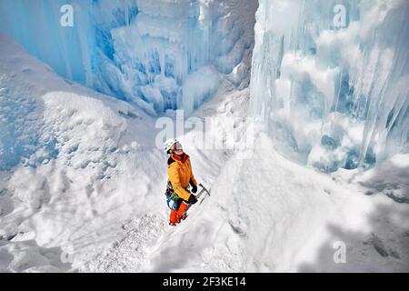 Frau Kletterin in oranger Jacke mit Eispickel in der Nähe von gefrorenen Wasserfall in den Bergen in Almaty, Kasachstan Stockfoto