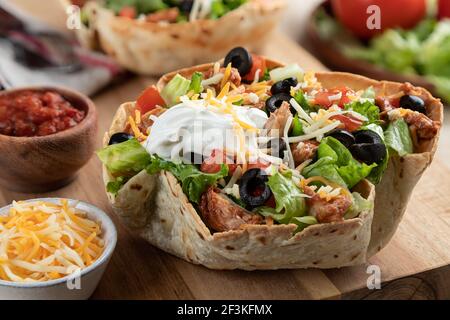 Nahaufnahme eines Taco-Salats mit Huhn, Salat, Tomaten, schwarzen Oliven, Käse und saurer Sahne in einer Tortilla-Schale Stockfoto