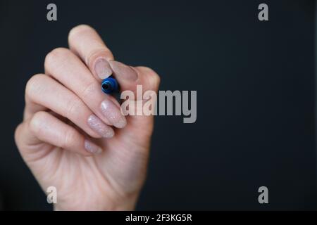 Weibliche Hand mit blauem Whiteboard-Marker auf schwarzem Hintergrund Stockfoto