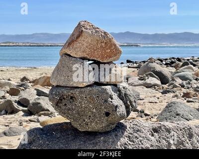 Eine Nahaufnahme von mehreren gestapelten großen Felsen am Strand Mit dem Wasser im Hintergrund und blauem Himmel Stockfoto