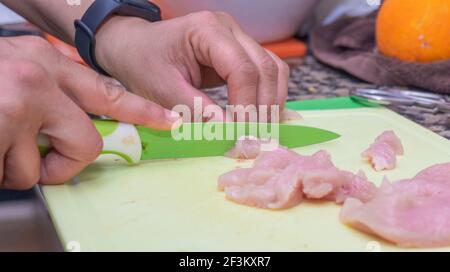 Ein selektiver Fokus Schuss von Händen schneiden Hähnchenfilets mit Ein Messer auf einem Schneidebrett Stockfoto