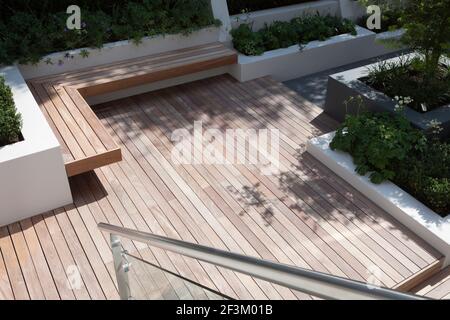 Eine Reihe von gerenderten und bemalten Stützmauern und Hochbetten. Hartholz-Terrassenbereich mit schwimmender Bank. Sitzecke. Hofgarten in Hampstead, Stockfoto