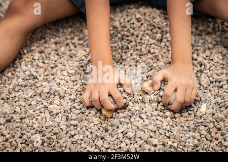 Kleiner Junge spielt beim Sammeln kleiner Steine. Kreative Outdoor-Aktivitäten für Kinder. Die Hände Kind spielt mit dem Kieselstein auf dem Boden. Stockfoto