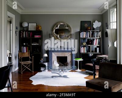 Wohnzimmer mit Bücherregale, Kamin und runden Spiegel mit Glas Couchtisch und Stühlen in Französisch Wohnung Stockfoto