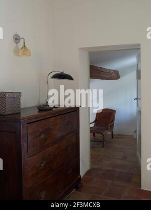 Kommode aus Massivholz, Lampe und Pendelleuchte mit offener Tür, um durch den Flur mit Deckenbalken und Terrakotta-Fliesenboden in residieren zu sehen Stockfoto