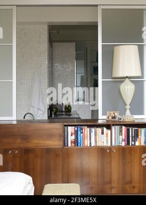 Bücher mit Blick durch offene Glas-Schiebewand zu Mosaik gefliesten Badezimmer in Wohnwohnung, USA. Stockfoto