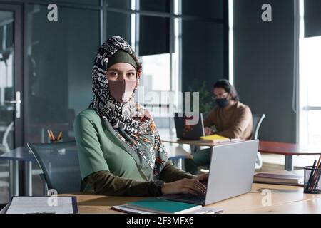 Porträt einer jungen muslimischen Frau, die während der Arbeit die Kamera anschaut Auf einem Laptop im Büro Stockfoto