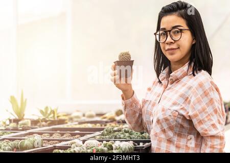 Authentische asiatische Frau lächelnd hält Kaktus in einem Kunststoff-Pflanzentopf im Kaktusladen. Konzept des Indoor-Gartenhauses. Stockfoto