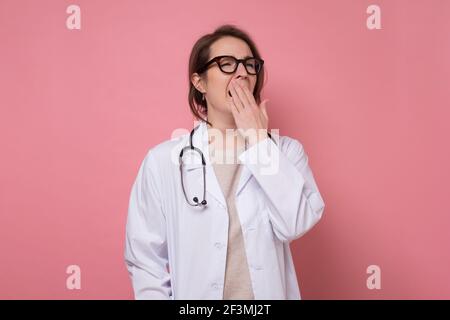 Junge schöne müde Arzt Frau trägt Stethoskop und Brille auf blauem Hintergrund gähnende Frau über den Mund mit der Hand. Unruhig und schläfrige Stockfoto