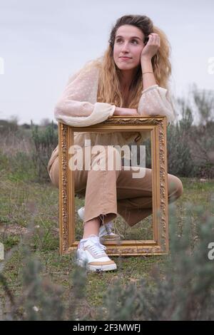 Künstlerisches Porträt einer blonden jungen Frau mit goldenem Rahmen in einem Feld. Fotografie im Retro-Stil. Stockfoto