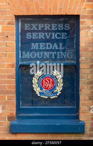 Glover & Riding Geschäft für militärische und zivile Schneider in Aldershot, Hampshire, England, Großbritannien. Express Service Medaille Montage Werbung im Fenster. Stockfoto