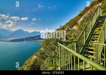 Panoramablick auf den Gardasee von der Busatte-Tempesta Weg in der Nähe von Nago-Torbole mit der eisernen Treppe, Torbole Stadt umgeben von Bergen in der Stockfoto