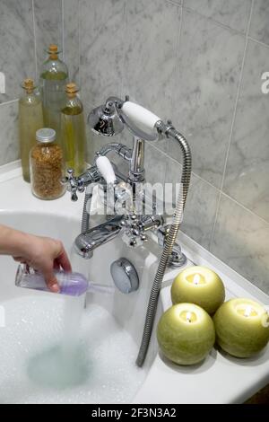 Person gießt Badeöl in die Badewanne mit Wasser aus Mischbatterie Stockfoto