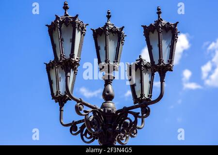 Vintage Eisen Straßenlampe aus schwarzem Metall geschmiedet mit figurigen Details Nahaufnahme gegen einen blauen Himmel an einem sonnigen Tag, niemand. Stockfoto