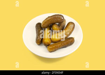 Gurken. Weißer Teller eingelegter hausgemachter Gurken auf gelbem Hintergrund. Stockfoto