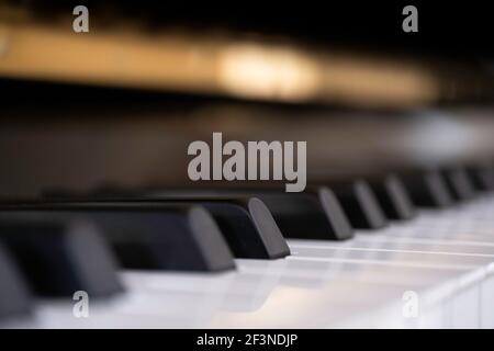 Seitenansicht von glänzenden schwarzen und weißen Klaviertasten mit der Reflexion des goldenen Messingrandes aus tiefem Winkel mit geringer Schärfentiefe. Konzentrieren Sie sich auf Stockfoto