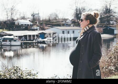 Stark schwangere blonde Frau, die einen Spaziergang am Fluss Stockfoto