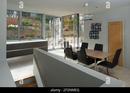Ein großer offener Bereich, eine Küche und ein Essbereich, mit Blick auf die großen großen Glaswandpaneele auf eine Terrasse. Minimalistische klare Linien und pl Stockfoto