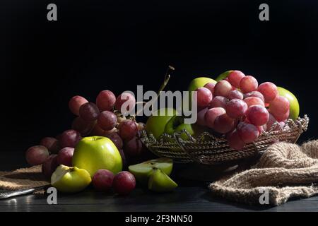 Trauben von rosa Trauben und grünen Äpfeln auf dunklem Hintergrund. Stillleben. Vitaminkorb. Speicherplatz kopieren. Stockfoto