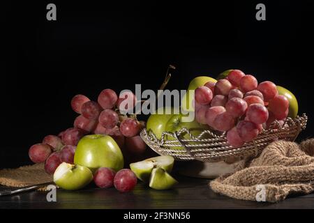 Trauben von rosa Trauben und grünen Äpfeln auf dunklem Hintergrund. Stillleben. Vitaminkorb. Speicherplatz kopieren. Stockfoto