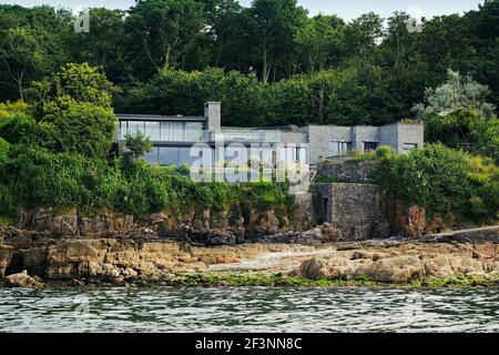 Blick aus dem Wasser von einem Meeresboden Clifftop modernes Haus von der Terrasse, Blick in den Hauptwohnraum. Große Glasschiebetüren öffnen sich. Boden bis Stockfoto