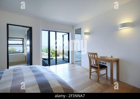 Die Innenräume eines modernen Hauses auf den Klippen mit Blick auf das Meer. Große Glaspaneele und Wände sowie Holzregale und Raumteiler. Ein Schlafzimmer Stockfoto
