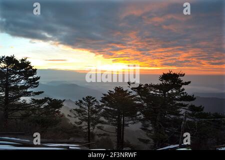 Bei Sonnenaufgang ragt die Sonne von hinter den Gipfeln der Berge aus, die Wolken werden mit einem fabelhaften, warmen Licht mit Kiefer im Hintergrund watchin beleuchtet Stockfoto