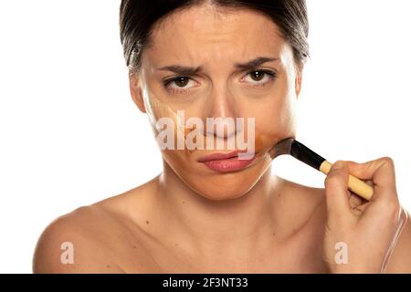 Junge nervöse Frau schmiert drei verschiedene Töne der flüssigen Grundlage Auf ihrem Gesicht auf weißem Hintergrund Stockfoto