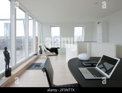Kein Unsinn, moderne Wohnung in Kopenhagen. Ein monochromes Dekor mit dezenten Farbakzenten. Ein Laptop auf einem Schreibtisch und einem Sitzbereich. Stockfoto