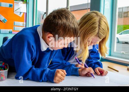 Grundschulkinder schreiben während einer Unterrichtsstunde auf einem Schreibtisch. Stockfoto