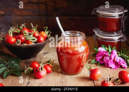 Ein Glas Rosenhüftgelee und frische Hagebutten auf einem Holztisch. Stockfoto