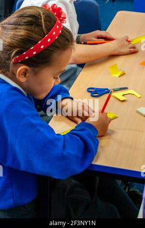 Grundschulkinder schreiben und schneiden Formen aus Papier auf einem Schreibtisch während einer Lektion. Stockfoto