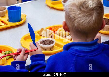 Kinder in einer Grundschule essen Schule Abendessen mit Plastiktellern, Tassen und Besteck. Stockfoto