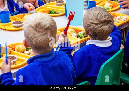 Kinder in einer Grundschule essen Schule Abendessen mit Plastiktellern, Tassen und Besteck. Stockfoto