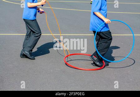 Grundschüler spielen mit Reifen draußen auf einem Schulhof während einer Pause vom Unterricht. Stockfoto