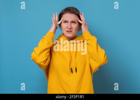 Kaukasische Frau hat Kopfschmerzen, die Finger auf den Schläfen halten. Studio auf blauer Wand. Stockfoto