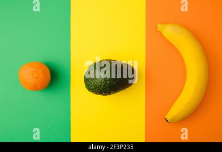 Clementine, Avocado und Banane auf einem grünen, gelben und orangefarbenen Hintergrund. Tropische Früchte flach Lay Idee. Stockfoto