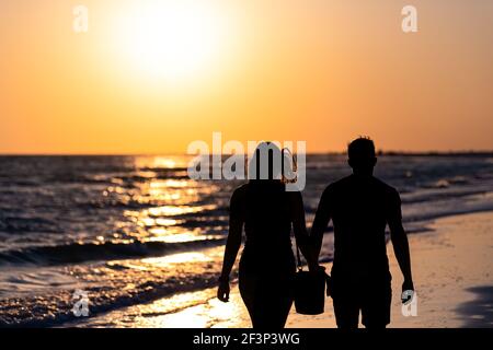 Sonnenuntergang Sonne in Siesta Key, Florida in Sarasota, USA mit Küste Ozean Golf von mexiko, junges Paar Silhouette zu Fuß am Strand, Hände haltend Stockfoto