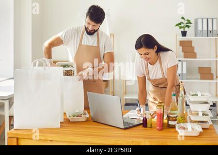 Positive junge Servicemitarbeiter, die mit Online-Bestellungen arbeiten Verpackung gesunde Mahlzeiten in Kisten Stockfoto