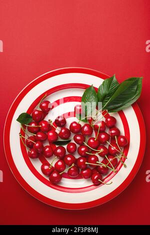 Frische Kirschen mit Blättern auf einem rot gestreiften Teller Stockfoto