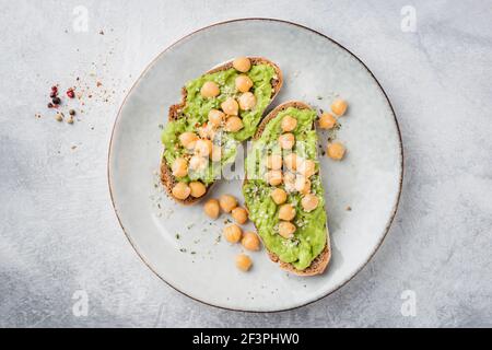 Roggenbrot Toast mit Avocado und Kichererbsen. Vegane vegetarische Snack oder Vorspeise, pürierte Avocado und Kichererbsen auf geröstetem Roggenbrot. Blick von oben, graues con Stockfoto